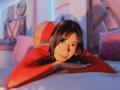 MelisaDaltonn, winking with red cheeks, lies on a bed in a red sweater, her ass raised, looking at the camera with a playful smile, in warm, colorful lighting.