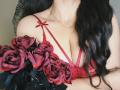Niferttiti with red lace bra, showing big tits, holding red roses with black leaves. Long black hair, gold necklace. Soft, sexy, and seductive.