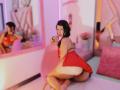 MelisaDaltonn in a red dress, kneeling with her ass up, looking back, wearing a pink hair clip, her tits and pussy visible, in a pink-lit room with mirrors.