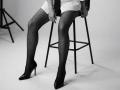Diantrisy's legs are in fishnet stockings, wearing black high heels, sitting on a stool. Her white skirt is up, her pussy is not visible. Black stool in background.