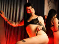 MaddyJacksson with black lace bra and thong, tattoos on arms and thighs, looking at camera, red light, mirror reflecting her back, long black hair, confident smile.