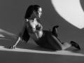 Black-and-white photo of MilagrosEdmisten with long ponytail, wearing lace bra and high-waisted skirt, lying on floor, legs bent, wearing black heels, showing her tits and ass.