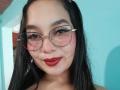 MelaniCoox has long black hair, red lipstick, and wears glasses with thick black frames. Her ass is not visible. She has light brown skin and a cute smile.