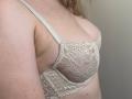 AlicePrings' small tits in a sheer, lace, beige bra, showing a bit of her pale skin and the bra's delicate, floral pattern. Her arm is partially visible.