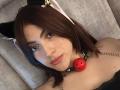 SpencerLe with brown hair, black cat ears, pink ribbon, and a red ball gag, looking at the camera with a neutral expression. She has a chain on her collar.