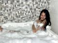 EstrellaXHot with long black hair, smiling, in a bubble-filled bathtub, naked, covering her tits with soapy foam, relaxed, in a modern bathroom.