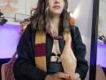 ArianaBlonde with wavy brown hair, wearing a black shirt and checkered scarf, holds a dildo with her right hand, showing a tattoo on her chest. Boobs visible.