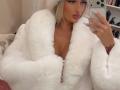 MademoiselleBella in a fluffy white robe, showing her tits, blonde hair, pink lipstick, and white nails, taking a mirror selfie with a phone.