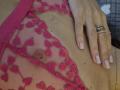 TenerliRize's pink lace lingerie with heart patterns, revealing a small, pink nipple. Her hand with a gold ring rests on her bare chest, nails painted pink.