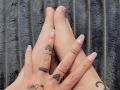 ElixirShanna's hands, pink nails, tattoos on fingers, black ink dots, black ink lines, crescent moon tattoo, black textured blanket, soft pink nail polish, relaxed, palms touching.