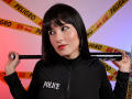 SkyeFrost with black bob, red lipstick, holding a Nikon camera over her shoulder, wearing a black police jacket, yellow "POLICE" tape in the background. Boobs not visible.