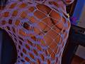 LorenLuv's large, round tits are visible through a purple, fishnet-style, open-weave top, showing dark nipples and a tattoo on her chest. Her brown skin is highlighted.