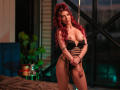 RubyMistique with red curly hair, wearing black strappy lingerie, exposing her tits, standing with hands crossed, in a dimly lit room with green and blue lights.