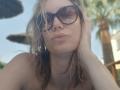 MissFrenchy with wet blonde hair, wearing dark sunglasses, pouting lips, and hand in hair, topless, showing small boobs, in a sunny outdoor setting with a palm tree.
