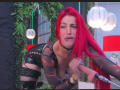 AlissaBrown with bright red hair, wearing a black sheer top and black leather shorts, leaning forward, holding a microphone, showing her tits, in a sexy, confident pose.