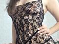 Strogoff in black lace lingerie, showing her tits through the patterned fabric. Her hand rests on her hip, fingers with white nail polish. Her brown hair falls to the side.