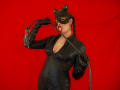 AdalinaVera in black latex cat mask, tight textured suit, holding whip, biting it, red background, full body, visible cleavage, long gloves, braided hair, slightly open mouth, seductive.