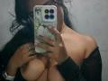IsabellaVoss taking a mirror selfie, showing her bare tits with a black sheer top, holding a phone with a cat case, wearing gold jewelry, and long black hair.