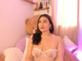 ElyRoss with long dark hair, wearing a sheer white lingerie top showing her tits, gold hoop earrings, sitting by a huge brown teddy bear, pink light.