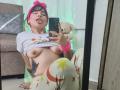 HairyValeri, with pink headband, tongue out, lifting shirt to expose her tits, wearing star-patterned pants, sitting in front of mirror, taking selfie with phone.