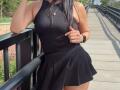 VivienneWest has a curvy ass in a black ribbed tank top and pleated skirt, leaning on a black rail with a thumbs-up, wearing a black watch.