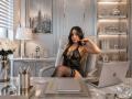 MindyLove with long brown hair, wearing black lace lingerie, garter, and stockings, sits in an office chair, finger on cheek, laptop on desk, sexy and confident.