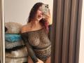 ValeryScot with curly red hair, wearing a black fishnet top, exposing her tits and showing a playful, open-mouthed expression in a mirror selfie. Her phone covers her face.
