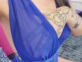 La robe bleu transparente de Shanna révèle ses petites seins et son bras tatoué de motifs en spirales et en étoiles. Ses mamelons sont légèrement visibles à travers le tissu..