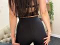 Stefanni with long brown hair, black sports bra, and black high-waisted leggings, showing her tight ass, hands on her butt, white bracelet, and red nails.