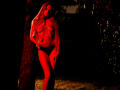 MiaMeowa with long blonde hair, red-lit, wearing a chain-strap top and black panties, standing by a tree, hand on hip, looking to the side, red highlights on skin.