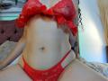 AlanaNaur has red lace bra and panties, showing her tits and pussy, with curly black hair, tattoos on her arms, and a light skin tone, sitting on a bed.