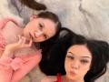 LornaAndGerry, two chicks with long hair, lying down, one in pink top with tits visible, other with black hair, pouty lips, both looking at camera, soft light.