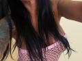 AndraD's black hair covers her pink fishnet top, exposing her small tits. She has a tattoo on her right arm. Her skin is tan.