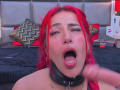 AlissaBrown with red hair, nose piercing, and black collar, mouth open, tongue out, being masturbated, visible dildo, slight facial cum, black bed, zigzag pillow, and sex toys.