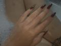 Dreia's hand with long, red, pointed nails resting on her wet, soapy tits in a bathtub. Her skin is tan, and a tattoo is partially visible.
