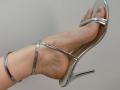 Tattiya's foot in a shiny silver high heel, showing a slight heel bruise and a visible ankle strap. Her toenails are neatly trimmed.
