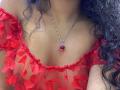 LightenStars with curly dark hair, wearing a red sheer floral top that shows her tits, and a silver necklace with a red gem. Her skin is light brown.