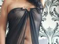 SexyMirra wearing a sheer black dress with a gold ring at the top, exposing her tits and a hint of her pussy. Her skin is tan, and she has curly black hair.