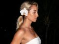 ViktoriiaLu with blonde ponytail, white orchid in hair, strapless white top, bare shoulders, brown earrings, side profile, looking to the right, dark background, night setting.