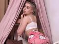 KrystalBerkovitch with blonde braids, white bra, and pink Hello Kitty panties, looking back with finger to lips, showing her ass and small tits.