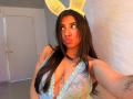 Celeste Morel, avec ses longs cheveux noirs, ses oreilles de lapin jaunes et ses lèvres pulpeuses, porte un haut en dentelle bleu transparent qui révèle ses grandes seins et a un tatouage sur son bras droit..