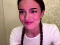 DrusillaMaiava has pink-tinted skin, brown braids, white shirt, pink lipstick, and a small nose piercing. She's smiling with pink eye makeup and a subtle chest visible.
