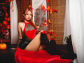 SuriEverly with red hair, heart-shaped red chest cutout, black fishnet arm, black shorts, knee-high black socks with red leaves, sitting on red velvet, autumn leaves, pumpkin.