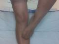 Le gambe abbronzate di EmiliaMilf, con calze marroni trasparenti, una gamba piegata al ginocchio, l'altro piede appoggiato su di essa, su un letto bianco con bordi blu..