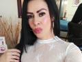 SofiMontes with black hair, pink lipstick, and white lace top, pouting her pink-tinted lips, wearing gold earrings and a necklace, holding a ring in a selfie.