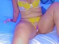 AuroraBenson wearing yellow lace bra and matching panties, sitting on a bed with her legs spread, showing her tits and pussy, with a pink dildo to her left.