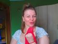 VeronikaGoldy with red panties in her hand, pouting lips, blue eyes, light brown hair in a ponytail, wearing a white polka dot shirt, green wall, wooden door.