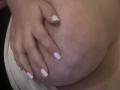 Barbarica's hand with white-painted nails rests on her large, round, bare tits. Her skin is light, and her fingers are gently pressed against her breast.