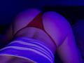 Olieri is on all fours, wearing a red thong and a striped top, with a purple and blue light illuminating her ass. Her skin is fair, and she's positioned downward.