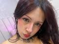 ValeryBeaumont has dark, wavy hair, freckled face, and red lips. She wears a black choker with stars, has hoop earrings, and a serious expression in a selfie.